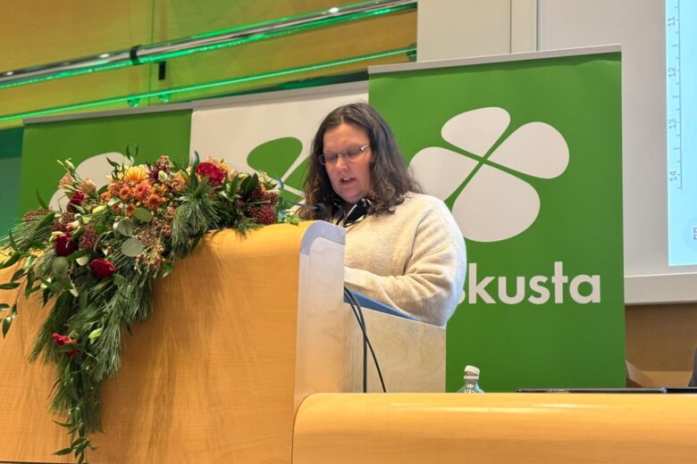 Naishenkilö puhujapöntössä Keskustan logo takana