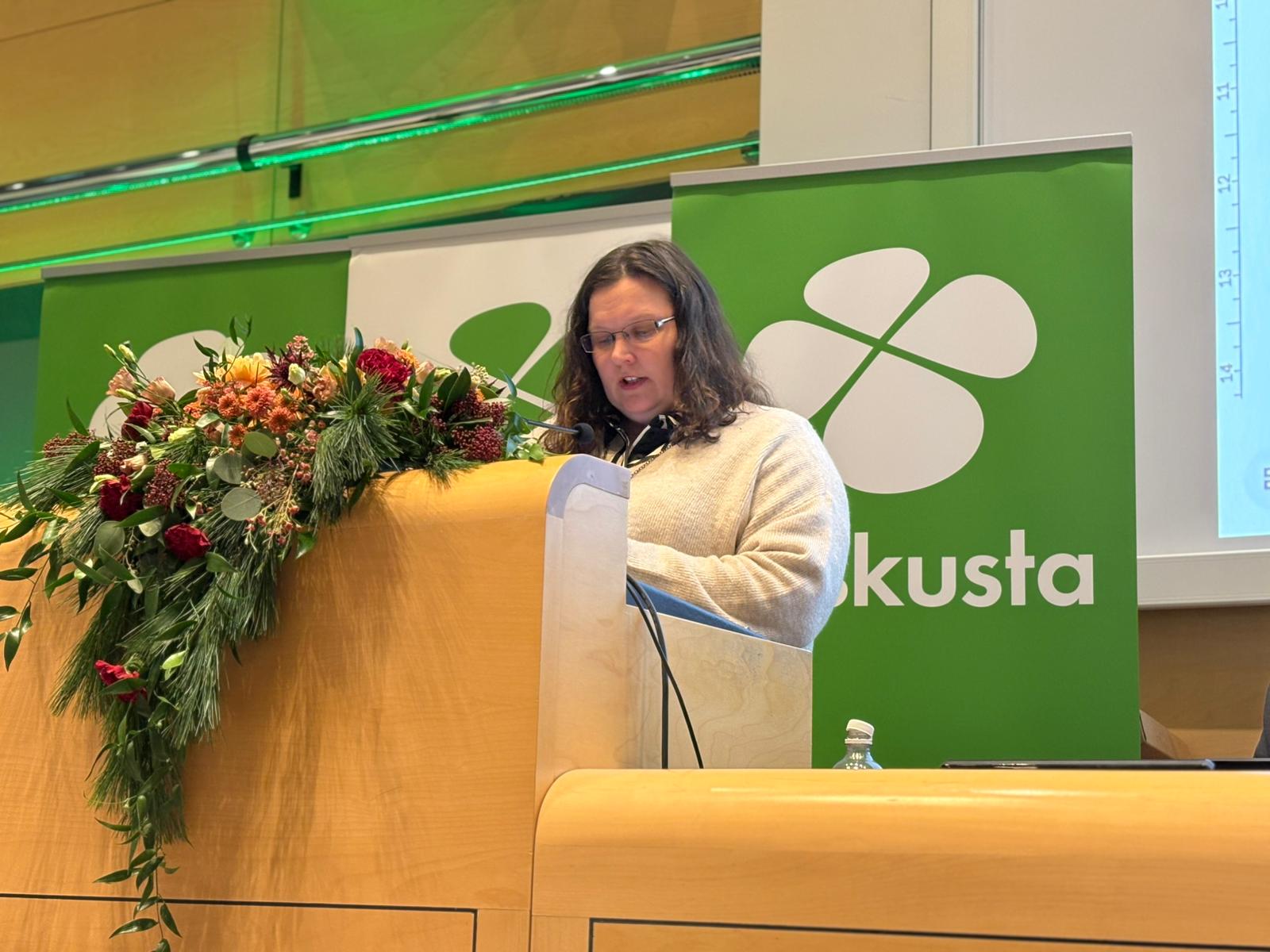 Naishenkilö puhujapöntössä Keskustan logo takana