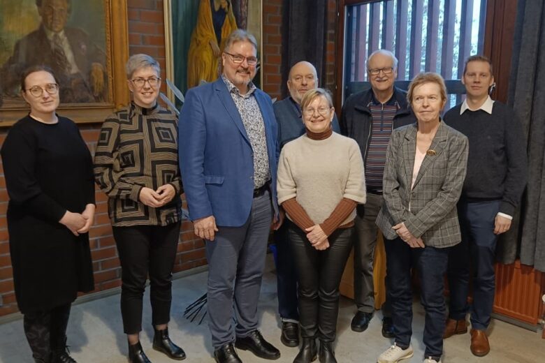 Ryhmäkuva jossa 8 ihmistä kuvattuna sisällä ikkunan vieressä.