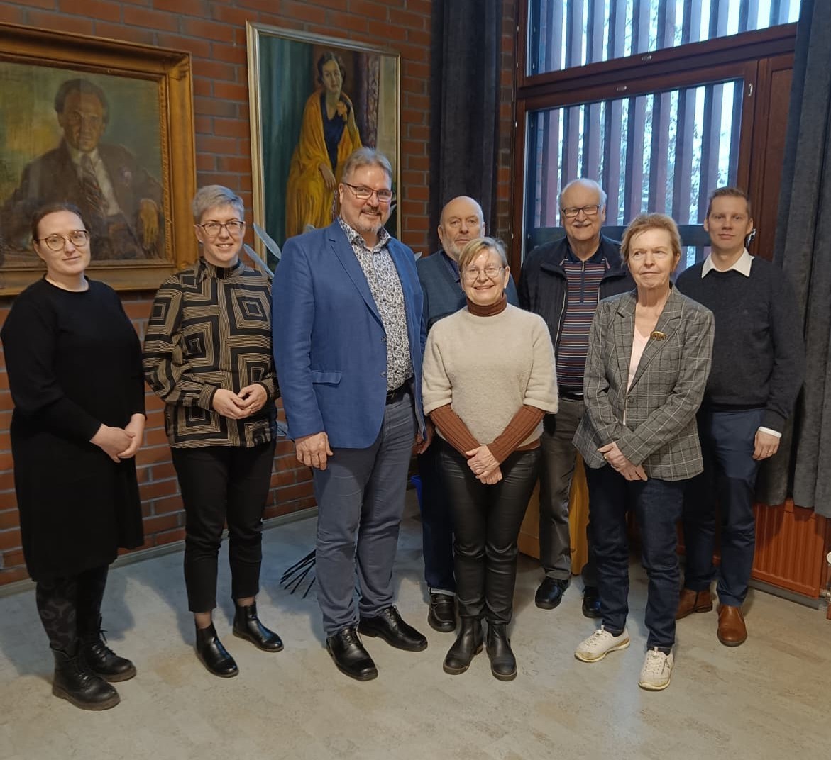 Ryhmäkuva jossa 8 ihmistä kuvattuna sisällä ikkunan vieressä.