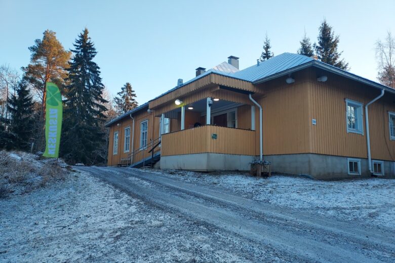 Teuron kylätalo talvisessa maisemassa ja vieressä Keskustan lippu.