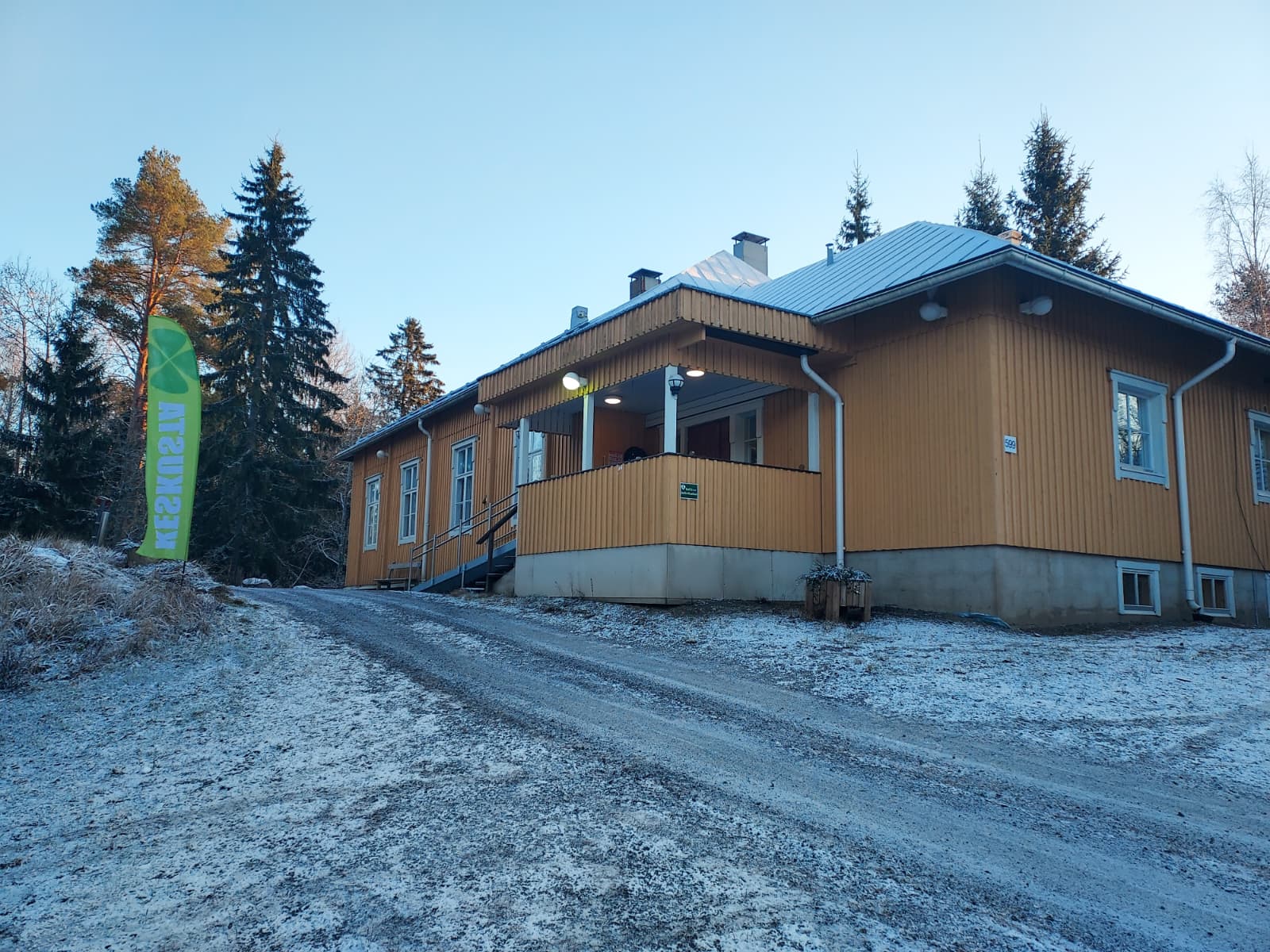 Teuron kylätalo talvisessa maisemassa ja vieressä Keskustan lippu.