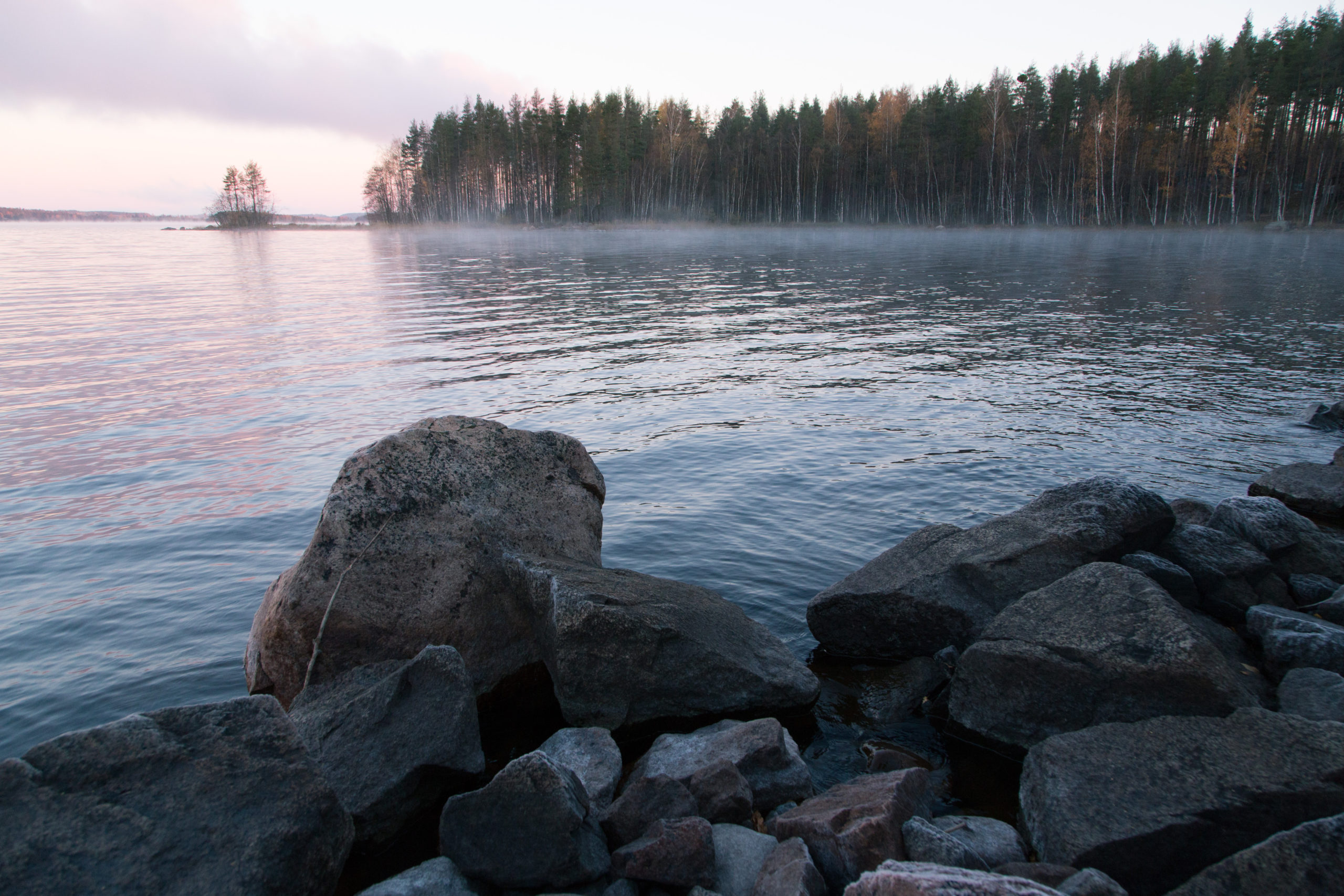 Rantakivikko auringonlaskussa, tyyni järvi.