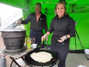 Seppo ja Elina paistavat lettuja vihreässä teltassa. Elinalla on paistinlasta kädessä. Tummat vaatteet molemmilla.