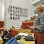 Maria Kaisa Aula seisoo ja pitää puhetta. Ruskeat housut. Harmaa paita. Tietokone on pöydällä. Takana näkyy valtuustosalin seinällä olevia entisten puheenjohtajian kuvia.