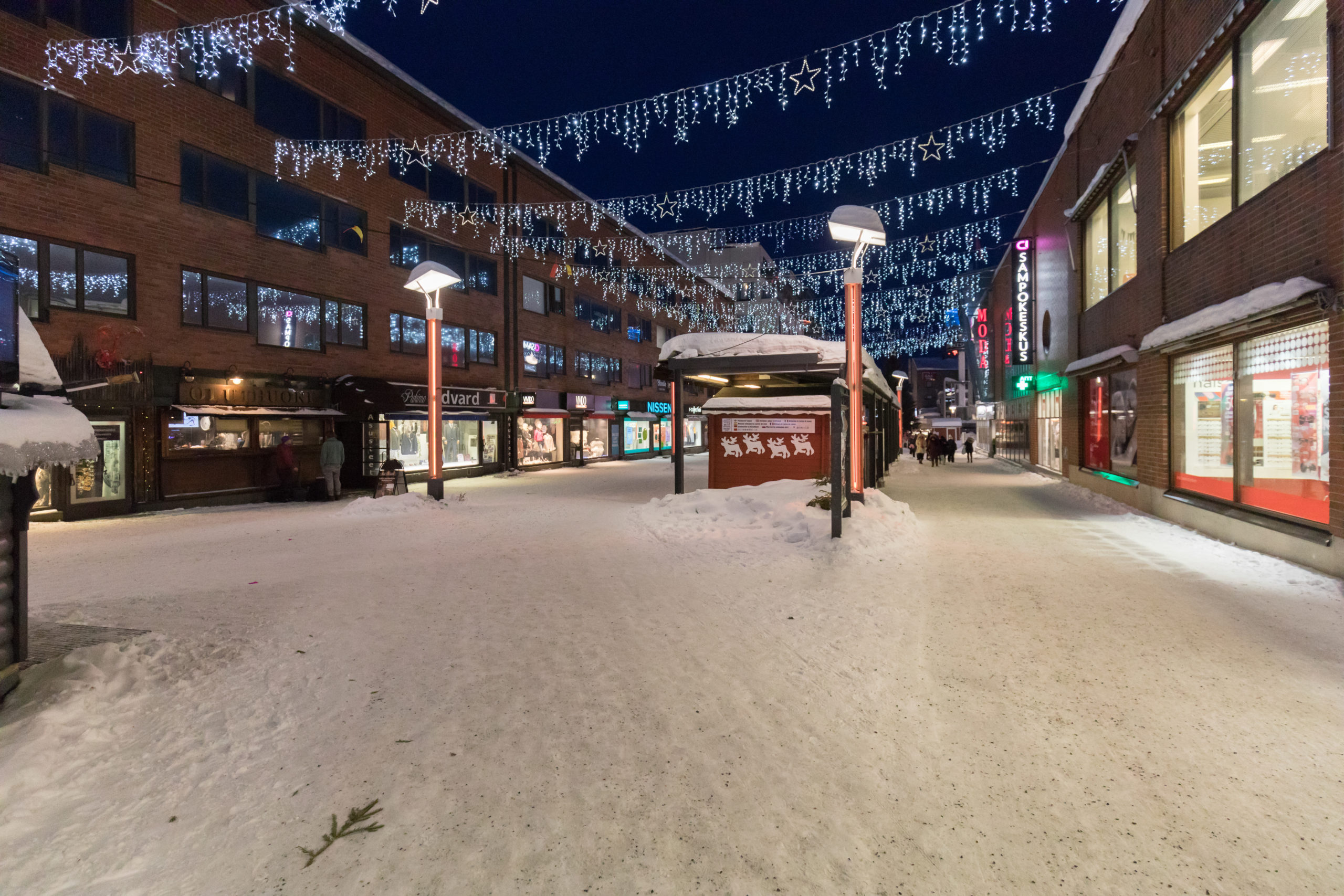 Rovaniemen keskusta iltahämärässä. Roikkuvia jouluvaloja ja luminen kävelykatu.